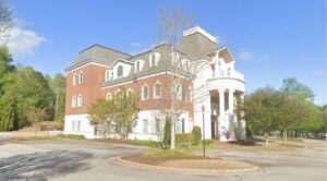 A grand exterior view of The Light of the World Church in Gainesville, Georgia, showcasing a multi-story red brick and white-columned building under a clear blue sky.