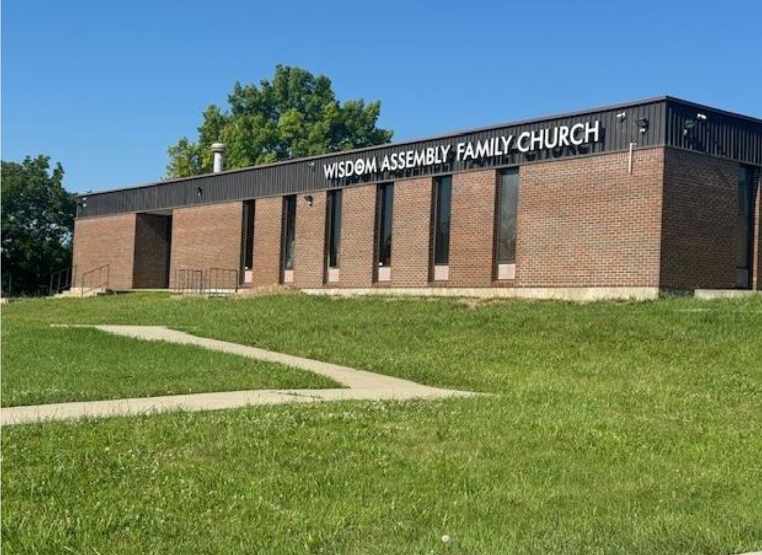 A brick exterior view of RCCG Wisdom Assembly Family Church in Kansas City, Missouri, taken under clear blue skies with a grassy foreground and bold church signage.